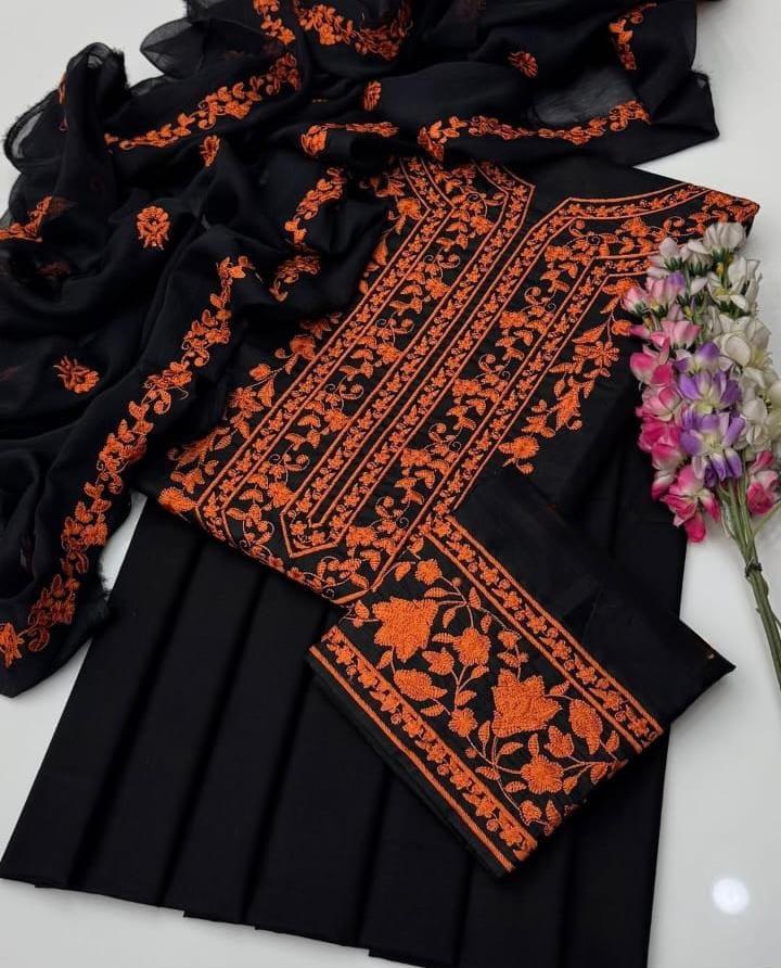 Black fabric with orange embroidery and a floral arrangement on a white background