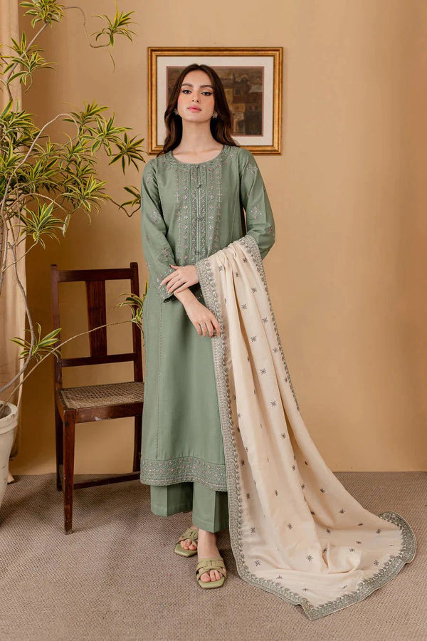 Woman in a green traditional outfit with a beige dupatta in a room with a plant and chair.