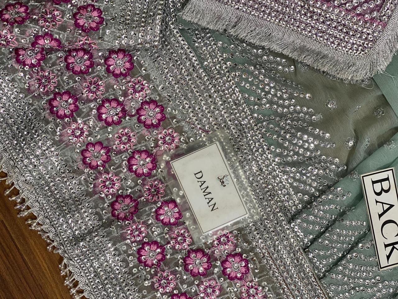 Decorative fabric with pink floral patterns and silver embellishments, featuring a brand label.