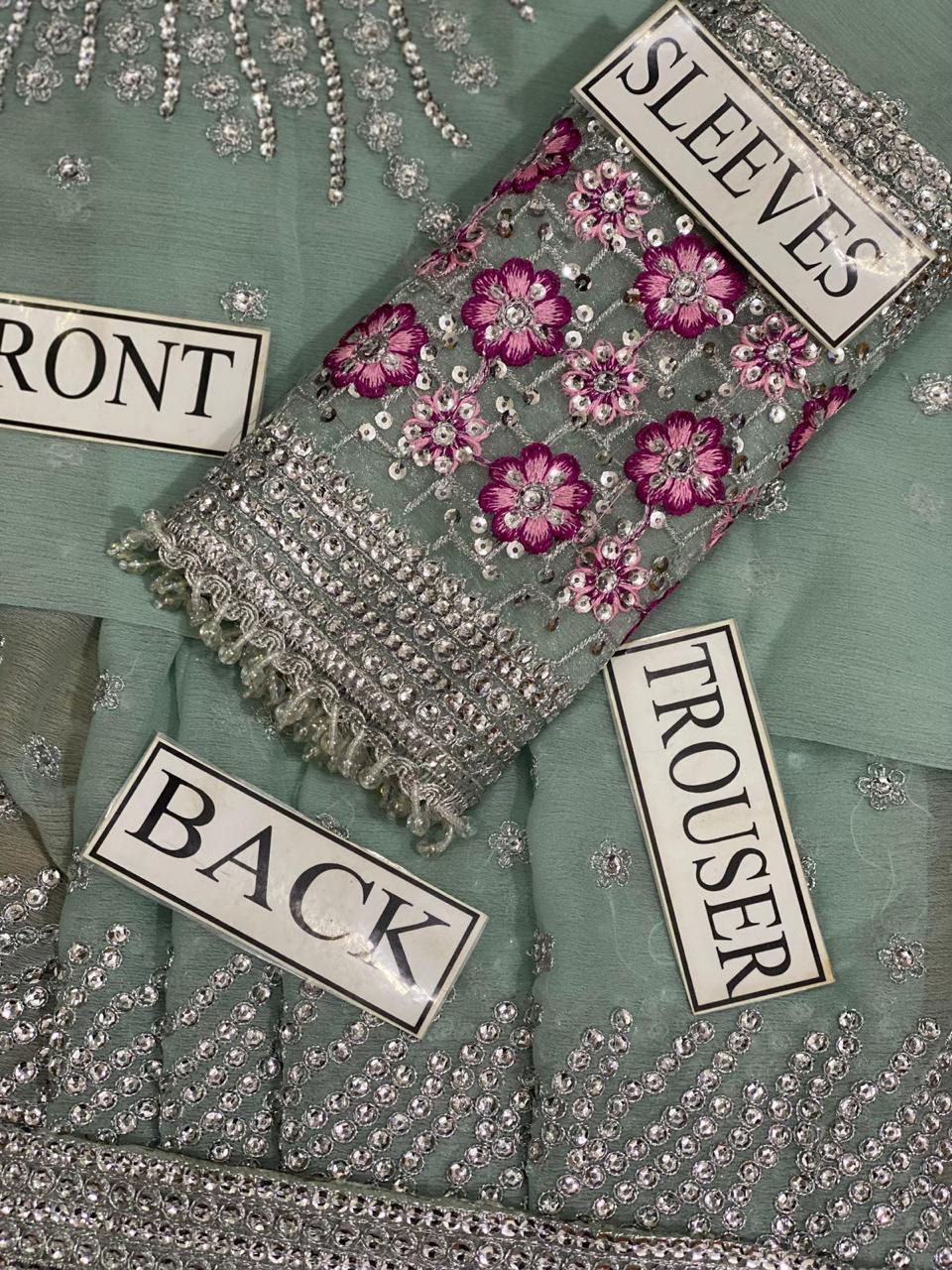 Embroidered fabric with floral patterns and labels indicating 'Front', 'Sleeves', 'Back', and 'Trouser' on a green background.