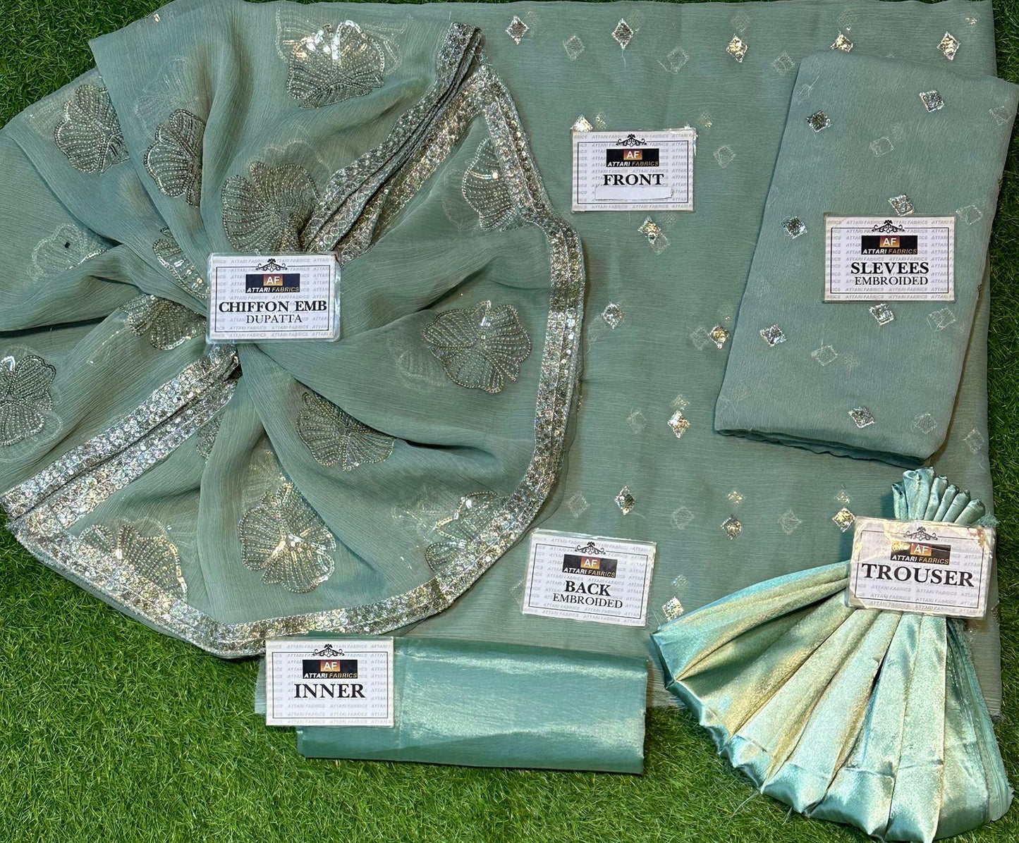Teal embroidered fabric set with labels on a grassy background