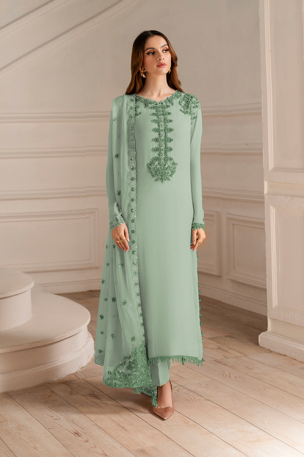Woman wearing a green embroidered outfit in an elegant room.