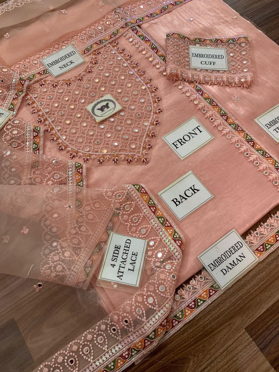 Detailed view of a pink embroidered garment with labeled parts on a wooden surface