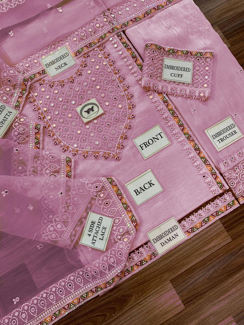 Pink embroidered garment with labeled parts on a wooden surface