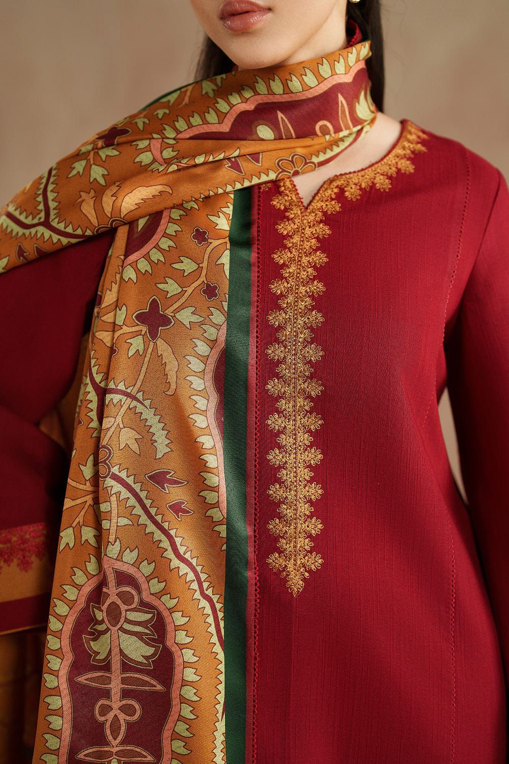 Red traditional outfit with gold embroidery and a patterned orange scarf.