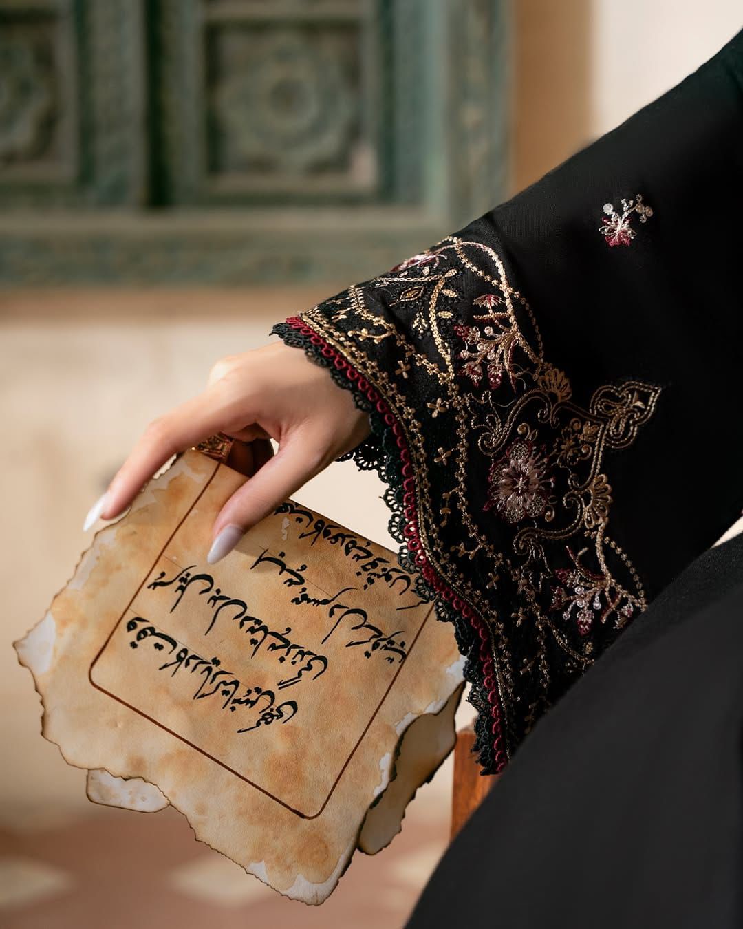 Hand holding a piece of paper with text, wearing a black embroidered sleeve.