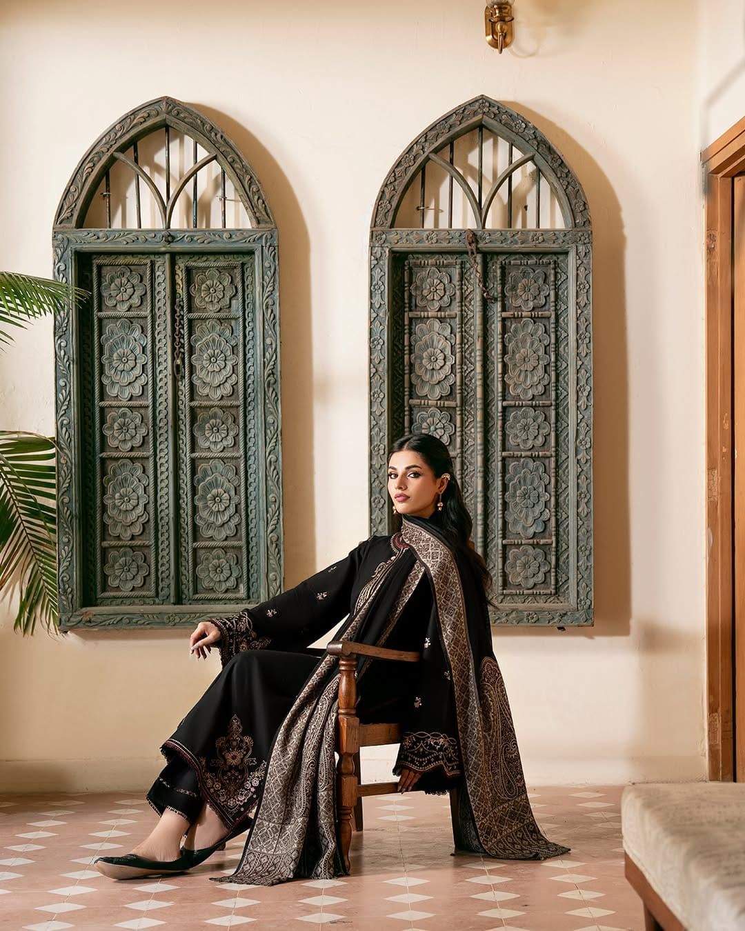 Woman in traditional attire sitting in a room with ornate windows.