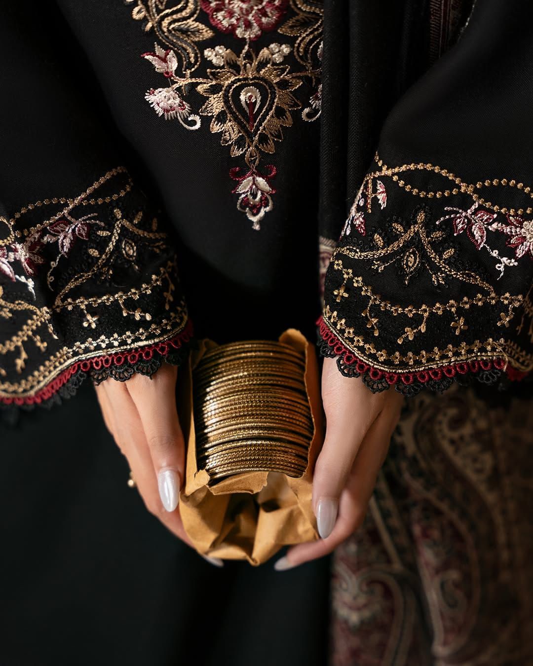 Person wearing intricately embroidered black garment holding a gold box.