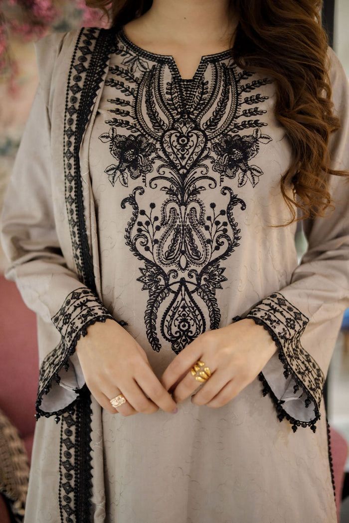 Close-up of a person wearing a light-colored outfit with intricate black embroidery.