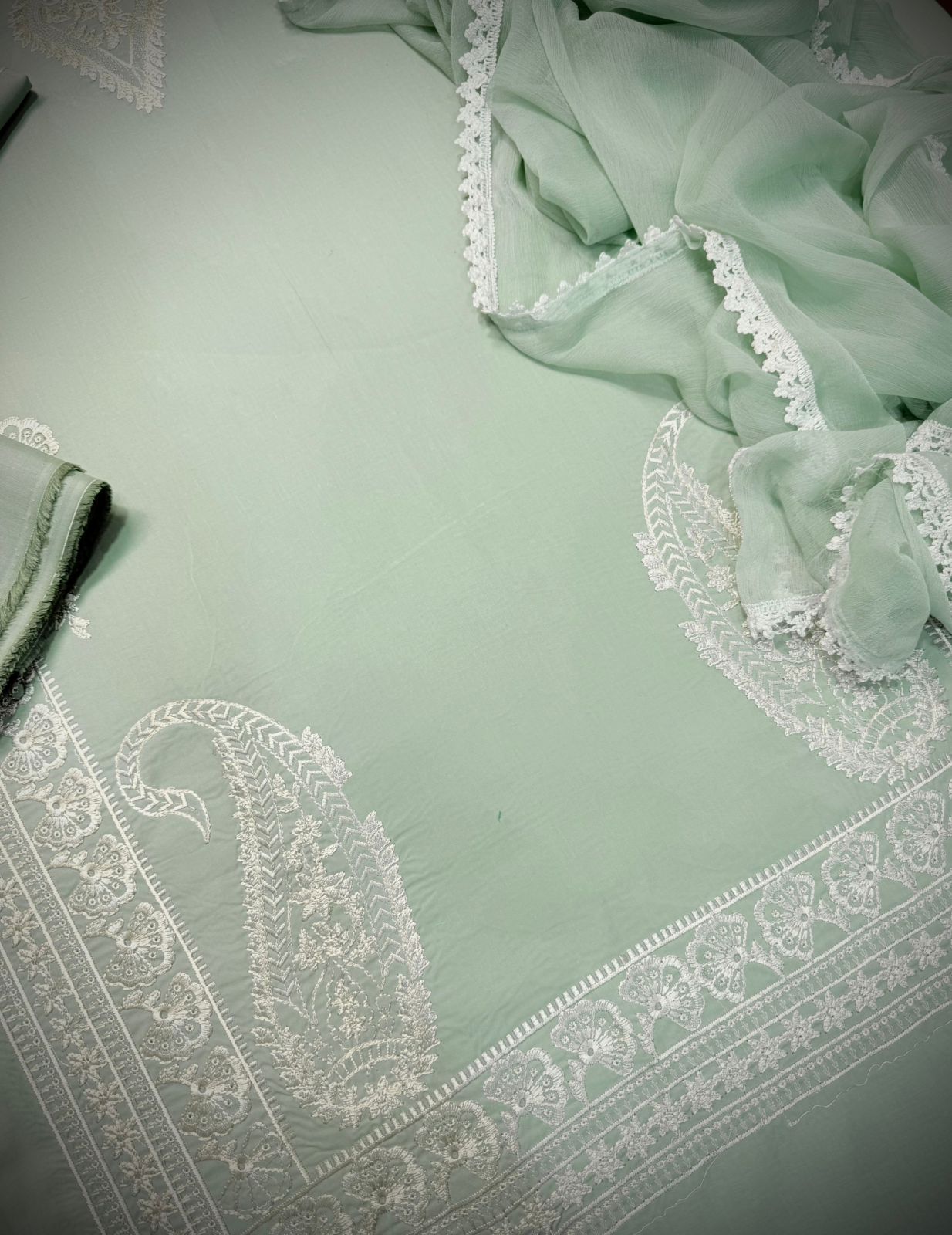 Light green fabric with white lace detailing on a light gray background