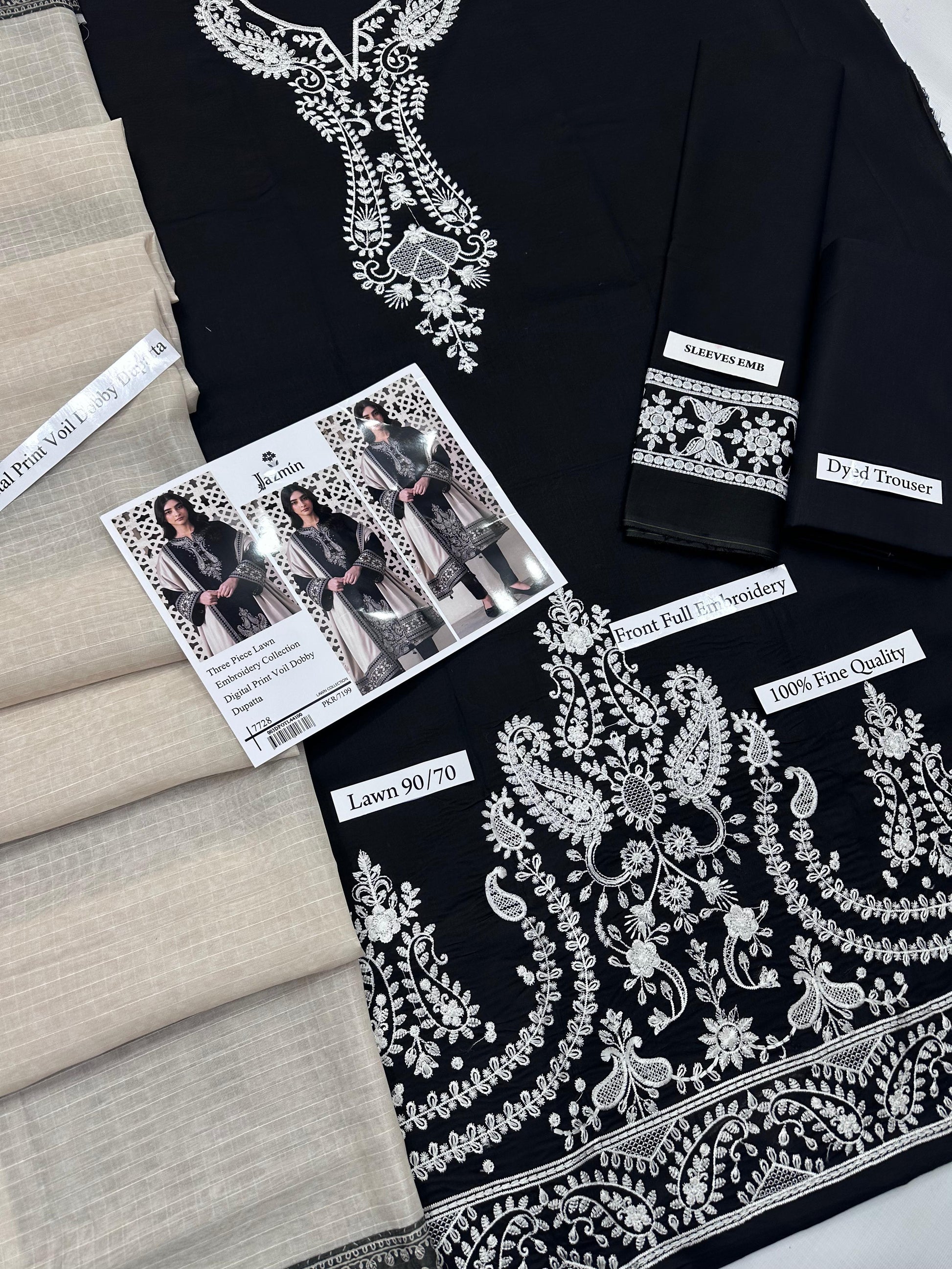 Black fabric with white embroidery and promotional material on a neutral background