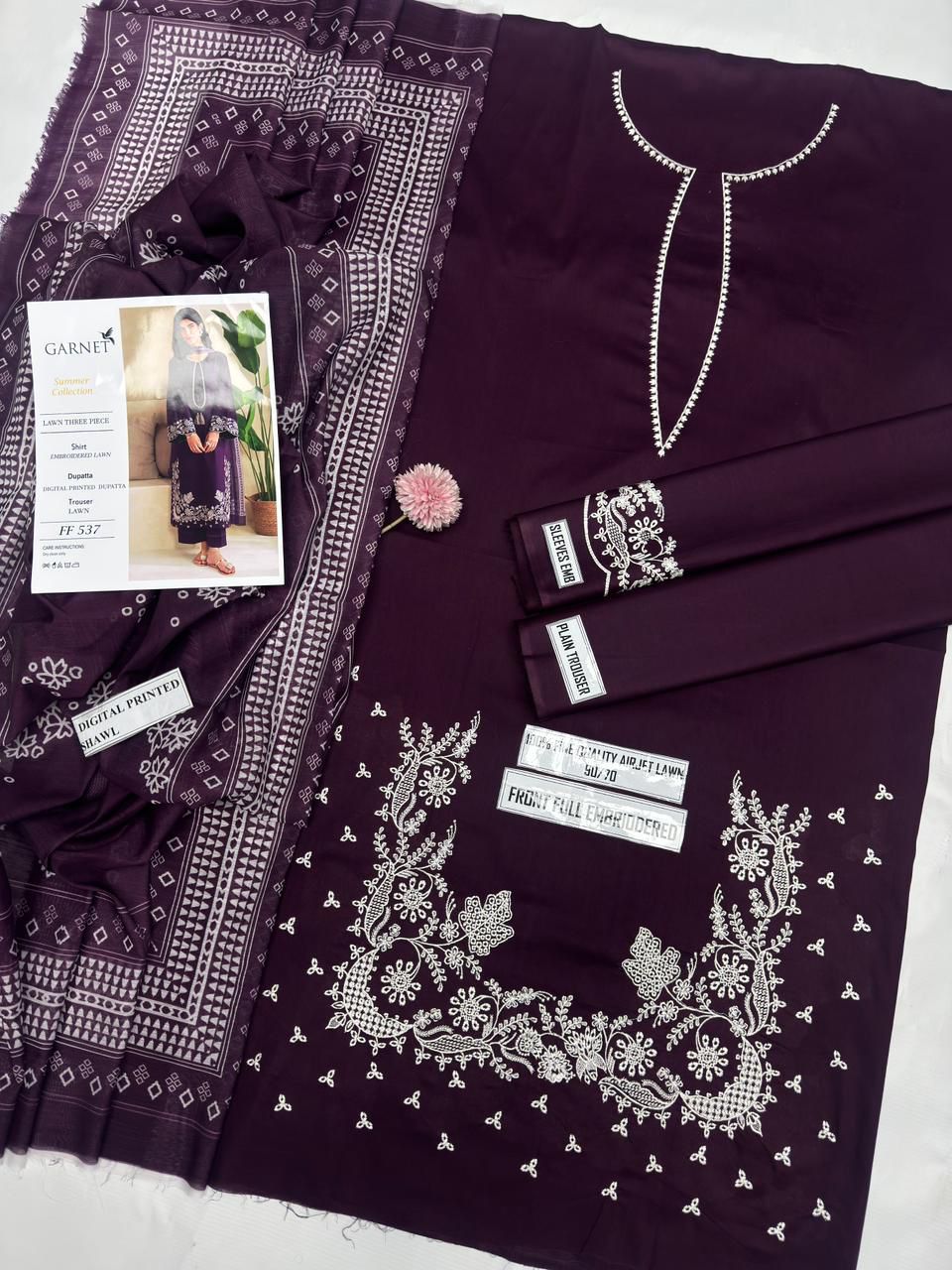 Purple embroidered garment with a magazine and pink flower on a white background