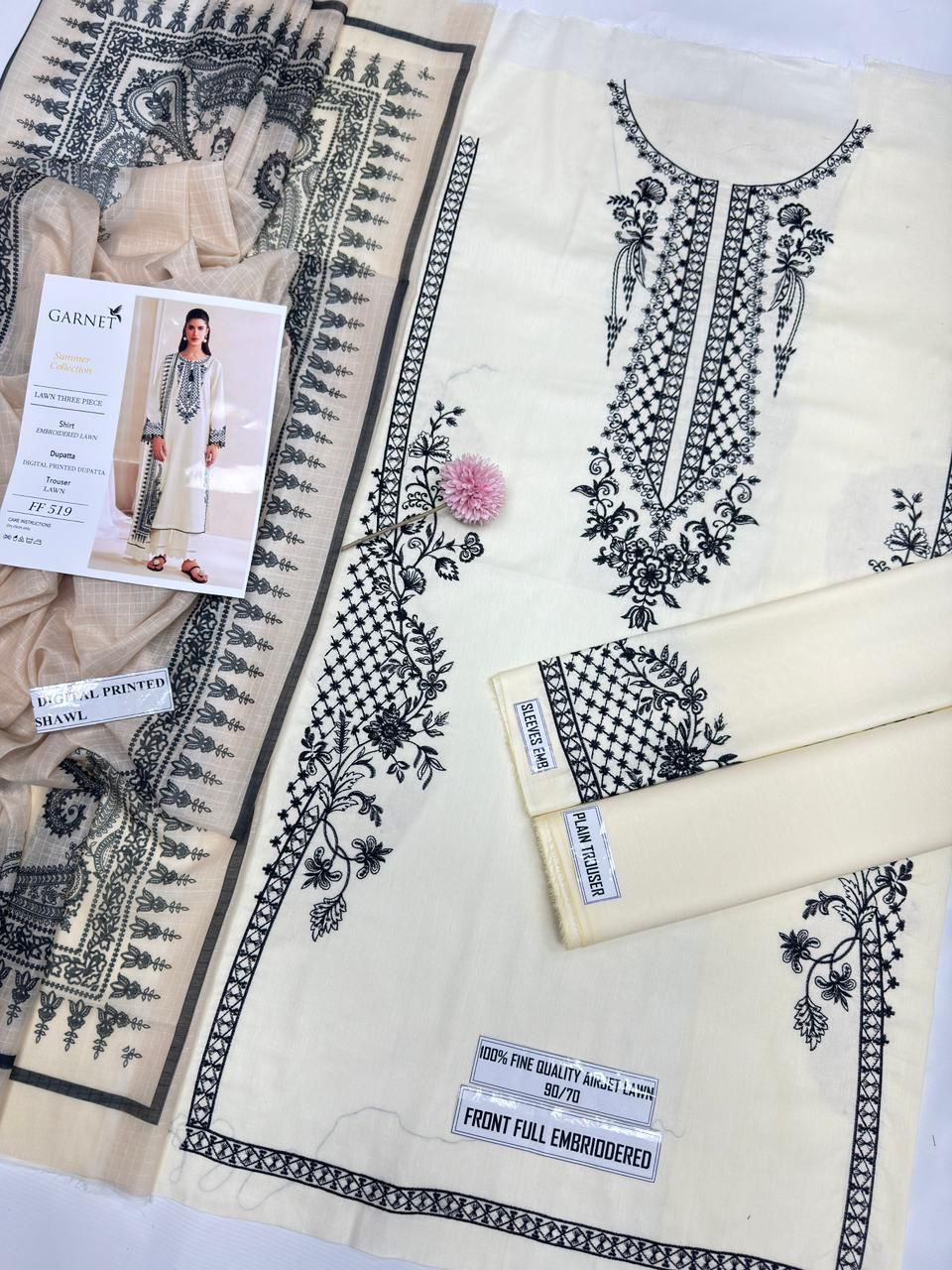 Embroidered fabric with black patterns on beige cloth, displayed with a model card.
