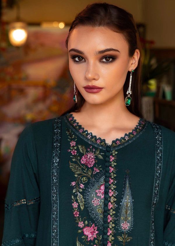Woman wearing a dark green embroidered top with floral patterns in a blurred indoor setting