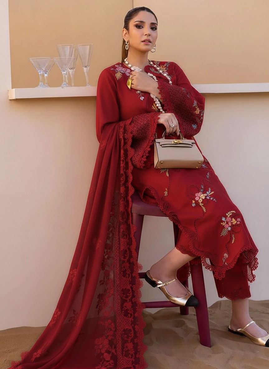 Woman in a red embroidered outfit sitting on a stool indoors.