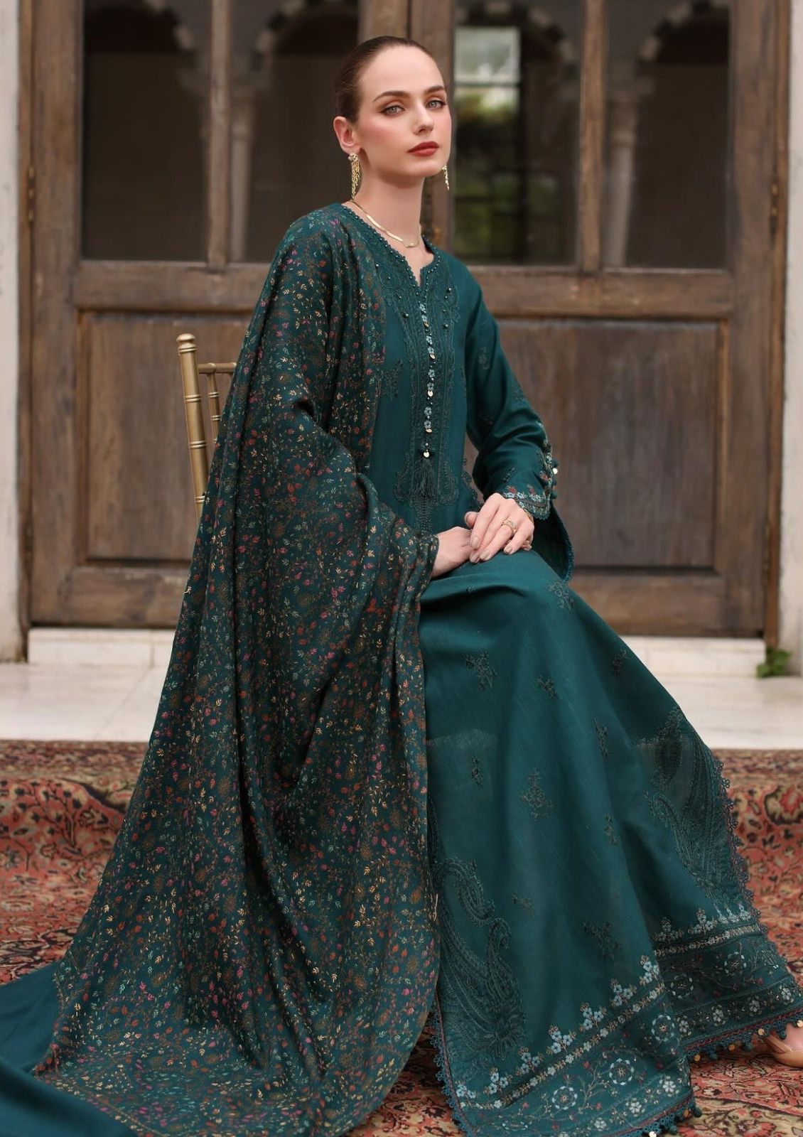 Woman in a teal traditional outfit with a matching dupatta sitting on a rug.