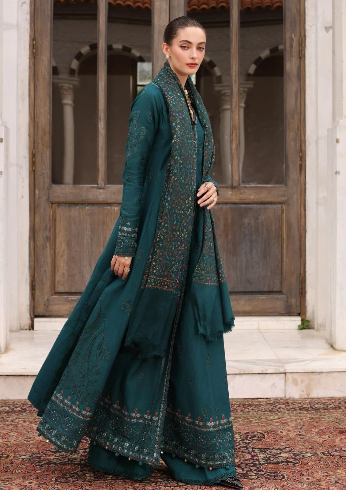 Woman in a teal traditional outfit standing in front of wooden doors.