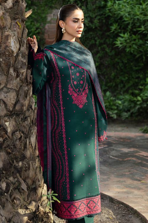 Woman in a green and red traditional outfit standing against a stone wall.