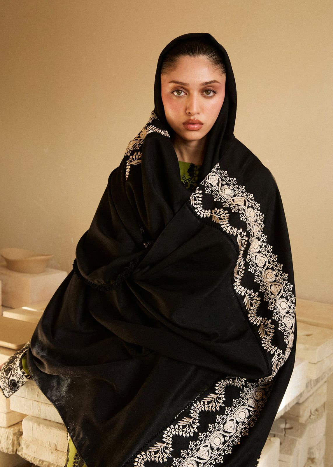 Woman wearing a black embroidered hijab sitting on a stone surface.