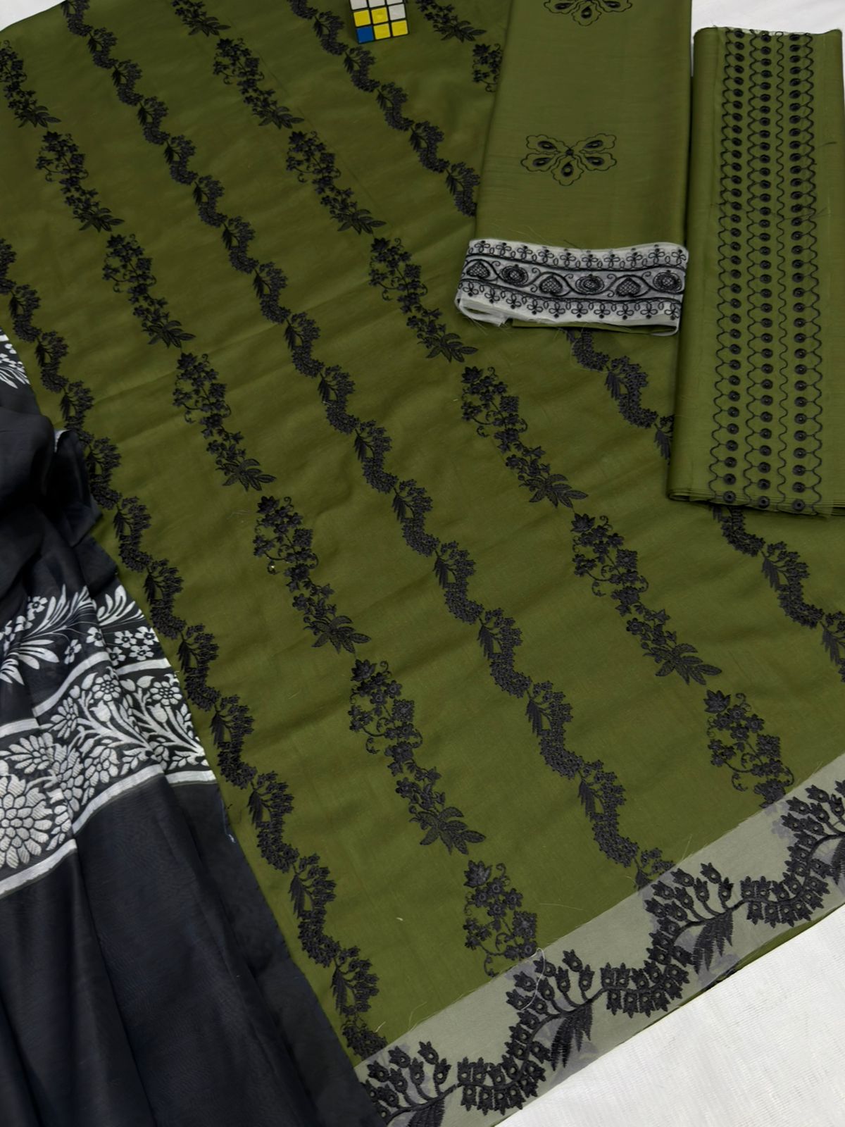 Green fabric with black floral patterns and a white border on a flat surface.
