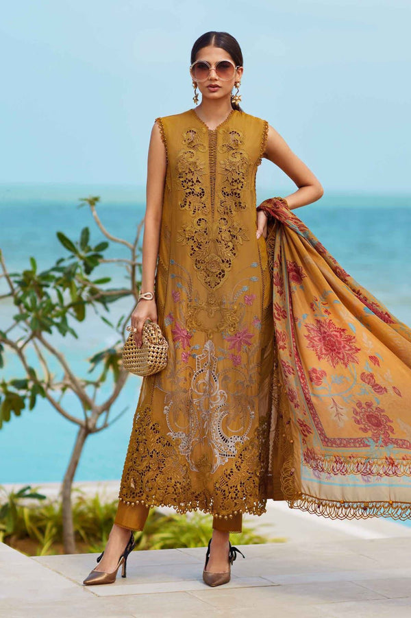 Woman in a mustard yellow embroidered dress with a floral scarf, standing by the ocean.