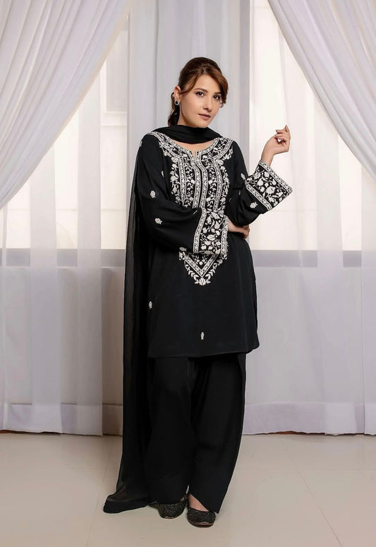 Woman wearing a black outfit with white embroidery in front of white curtains