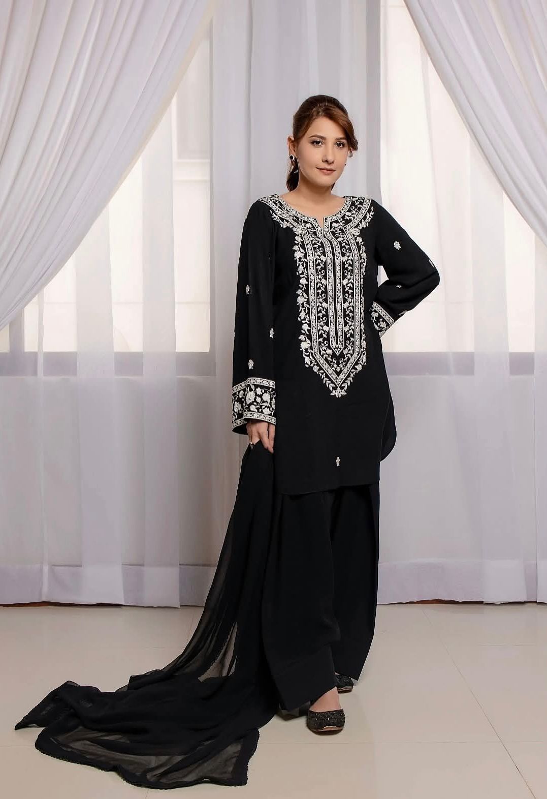 Woman wearing a black traditional outfit with white embroidery in a bright room.