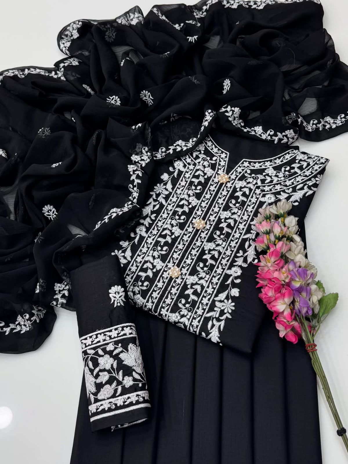 Black outfit with white embroidery and a floral arrangement on a white background