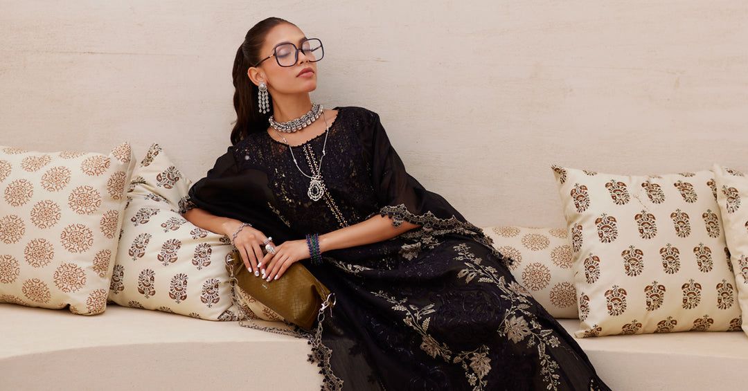 Woman in a black traditional outfit sitting on a patterned sofa.