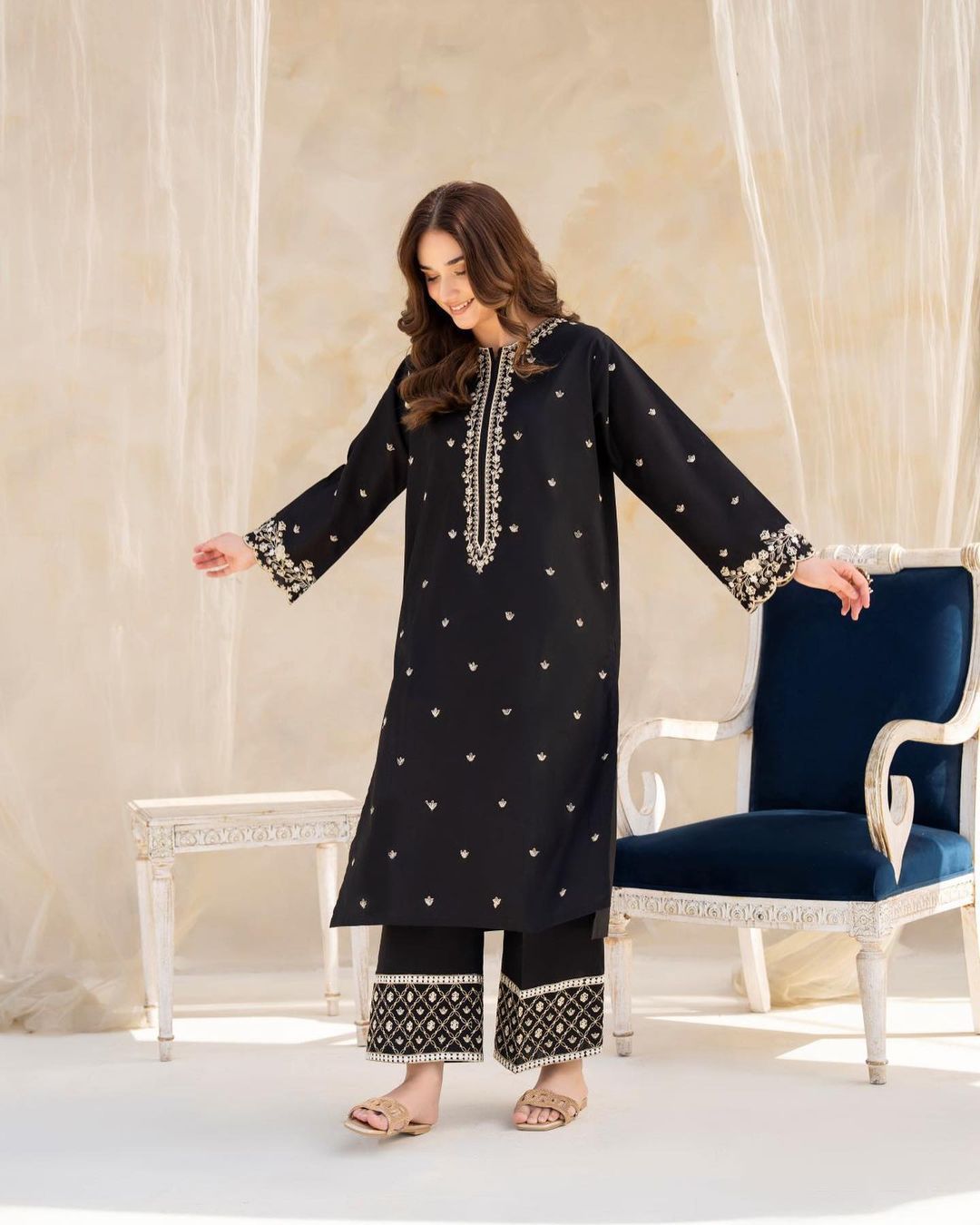Woman wearing a black embroidered outfit in a decorative room.