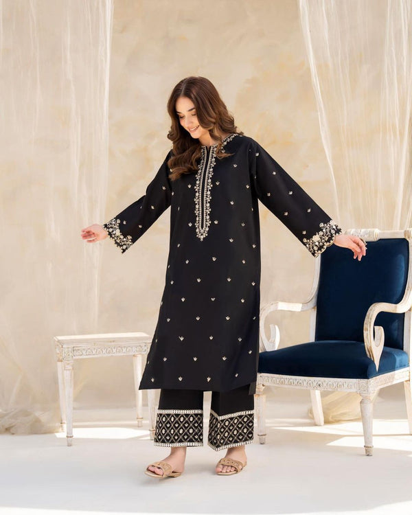 Woman wearing a black embroidered outfit in a decorative room.