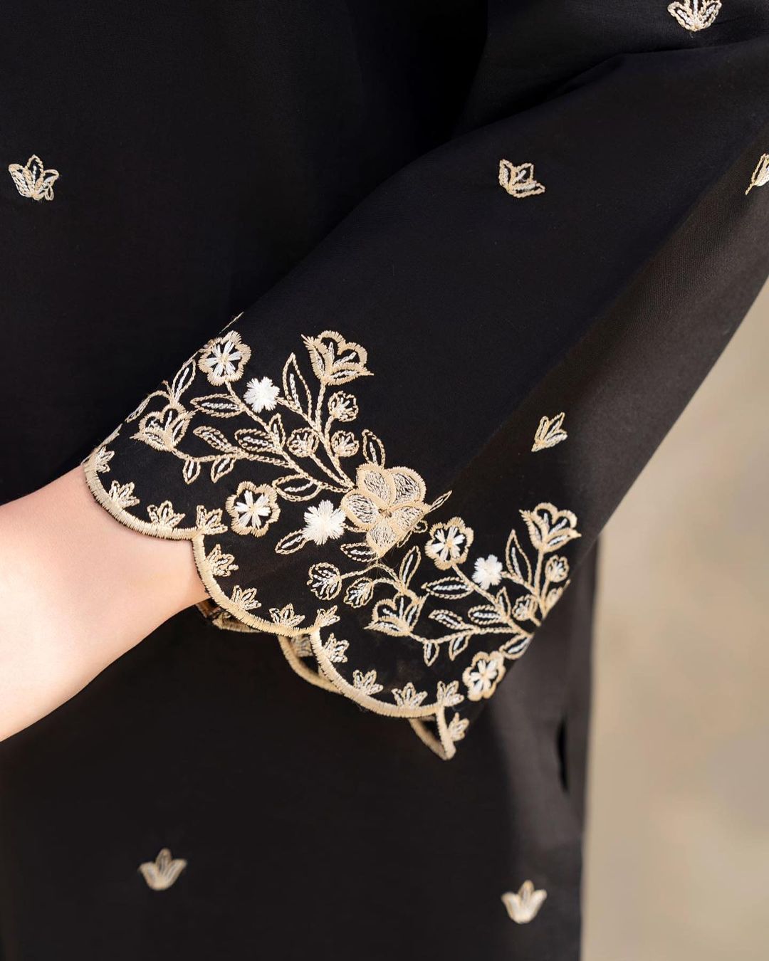 Black fabric with gold floral embroidery on a blurred background