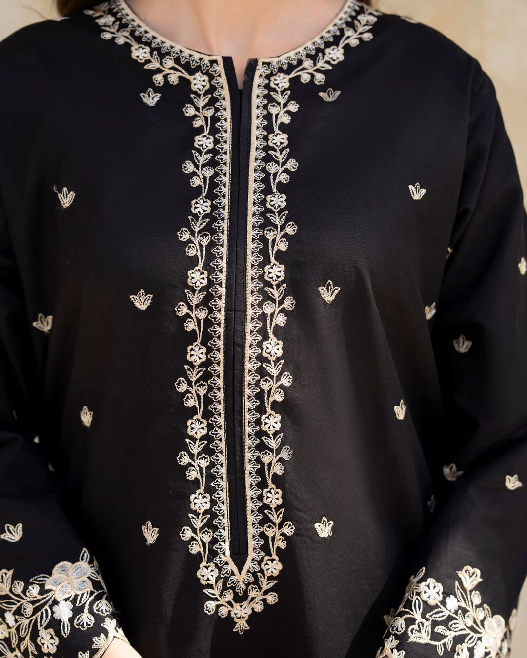Black garment with intricate white embroidery on a beige background