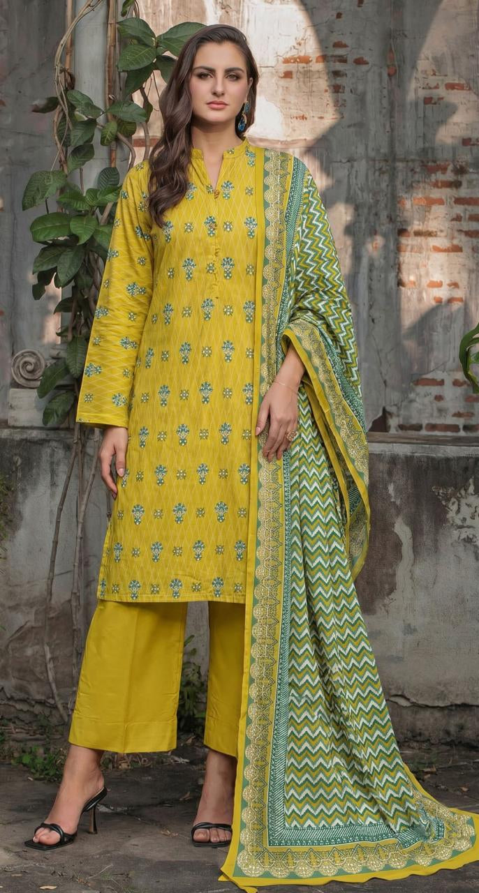 A woman modeling a three-piece printed lawn suit from Gul Ahmed Summer Collection in Yellow Earth Crust. The set includes a yellow kurta with green floral prints, a matching yellow pleated skirt, and a green printed dupatta.