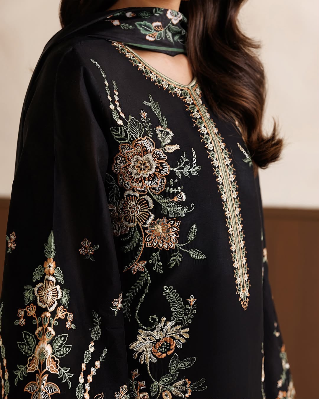 Black embroidered garment with floral patterns on a neutral background