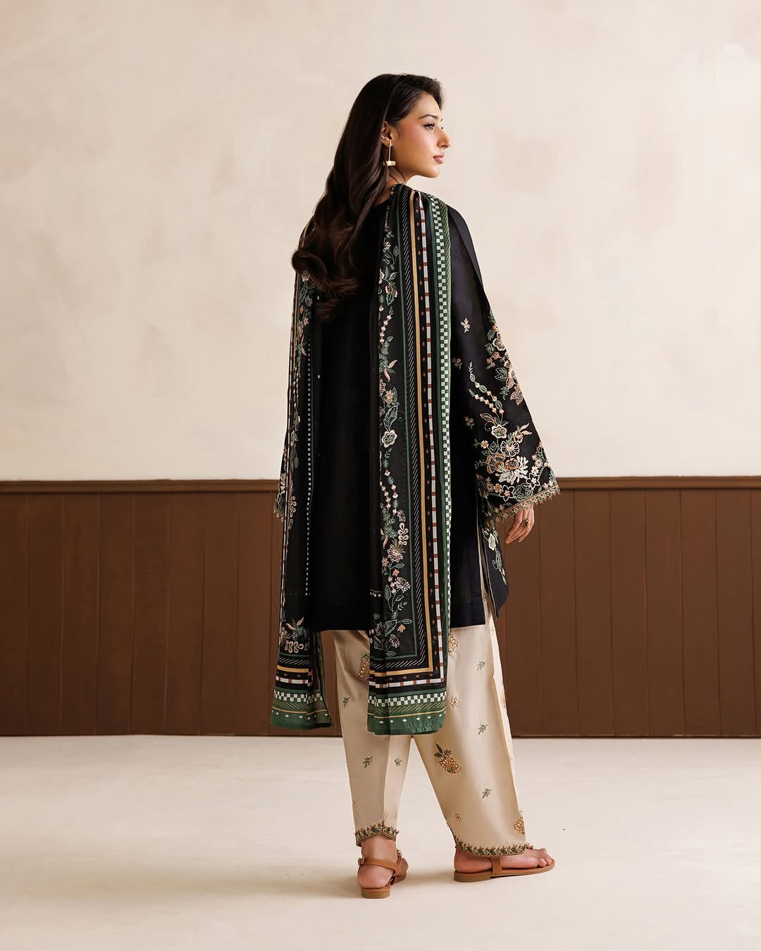 Woman wearing a black embroidered outfit with beige pants in a minimalistic setting